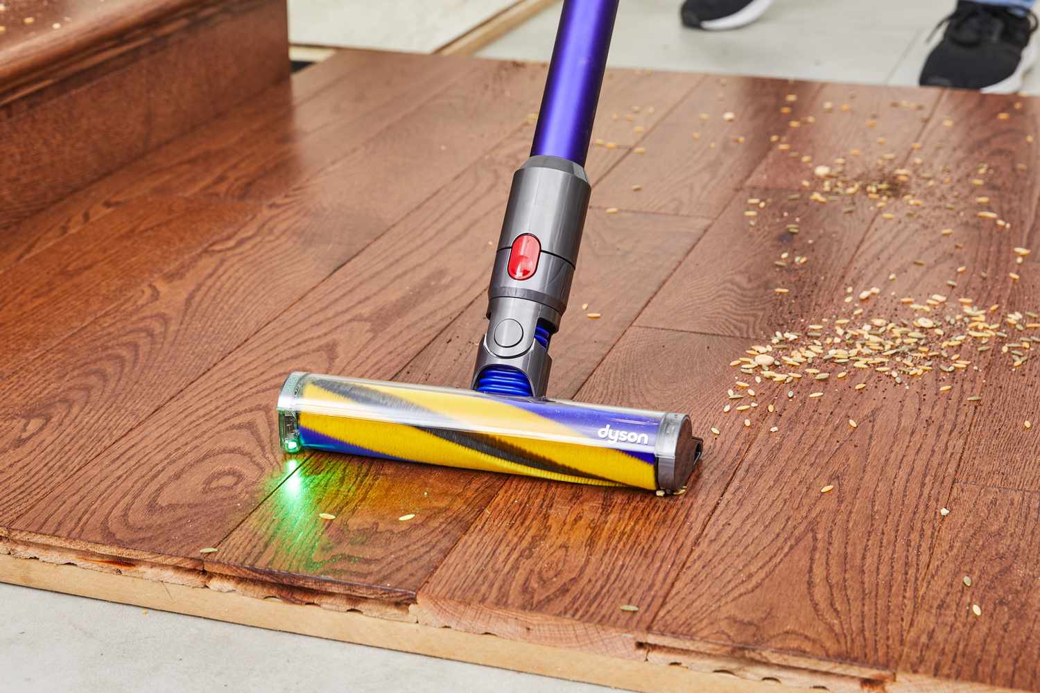 Zoomed in on the Dyson Gen5detect floor cleaning attachment, as someone uses it to vacuum a wood floor