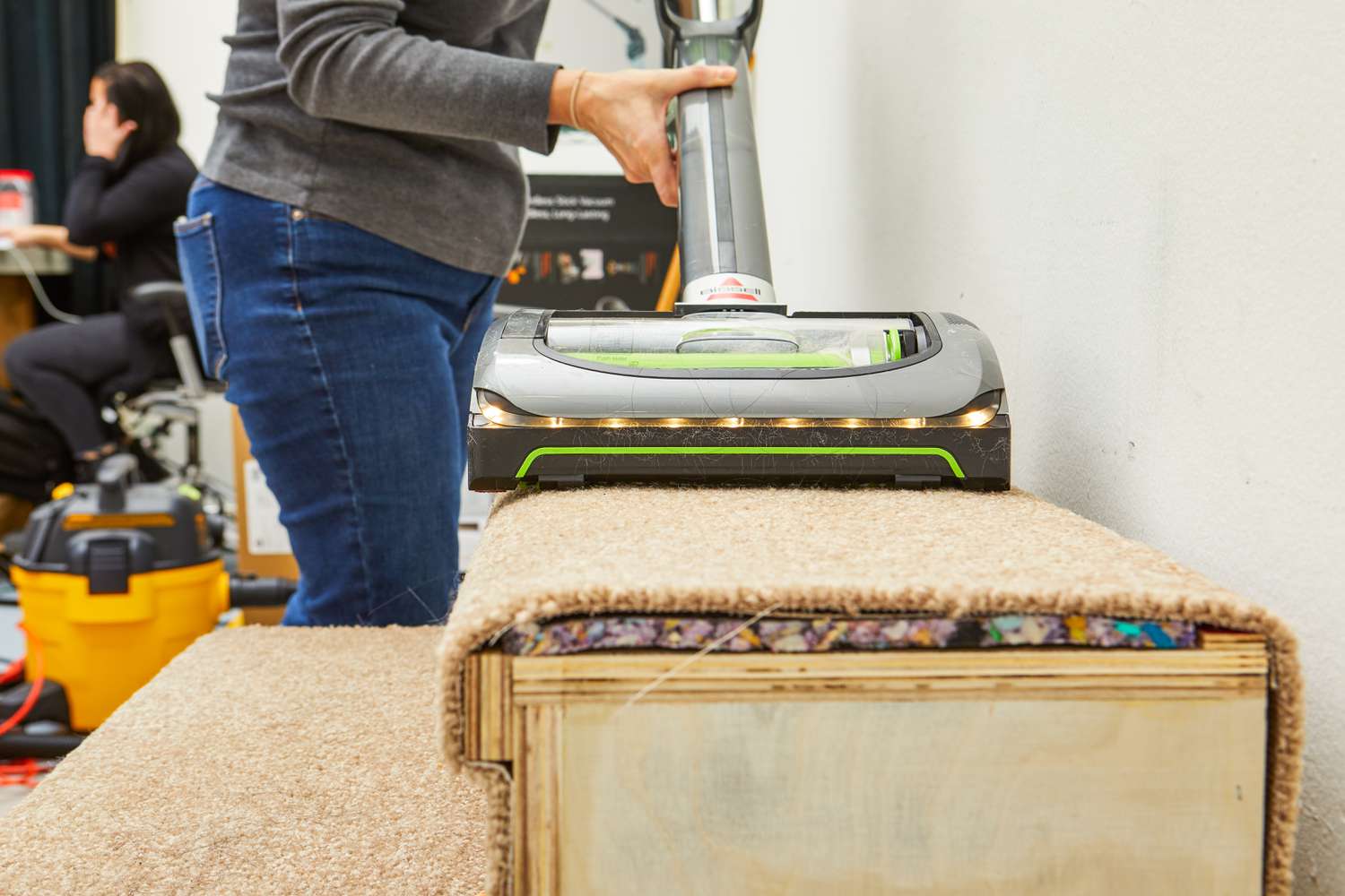 A person vacuums carpeted stairs using the Bissell 1984 Air Ram Cordless Vacuum.