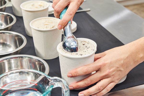 Person scooping ice cream from first in a line of ice cream pints in front of metal bowls