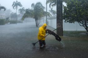 A man works to clear debris from a flooded street as heavy rain falls over parts of South Florida on Wednesday, June 12, 2024