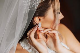 A beautiful bride fastens an earring. Close-up portrait of a beautiful girl in a wedding dress in the interior.