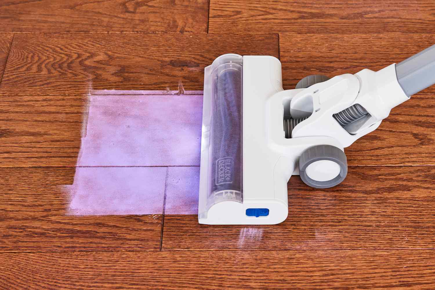 The Black + Decker Powerseries+ 16V MAX Cordless Stick Vacuum picking up purple powder from a wooden floor