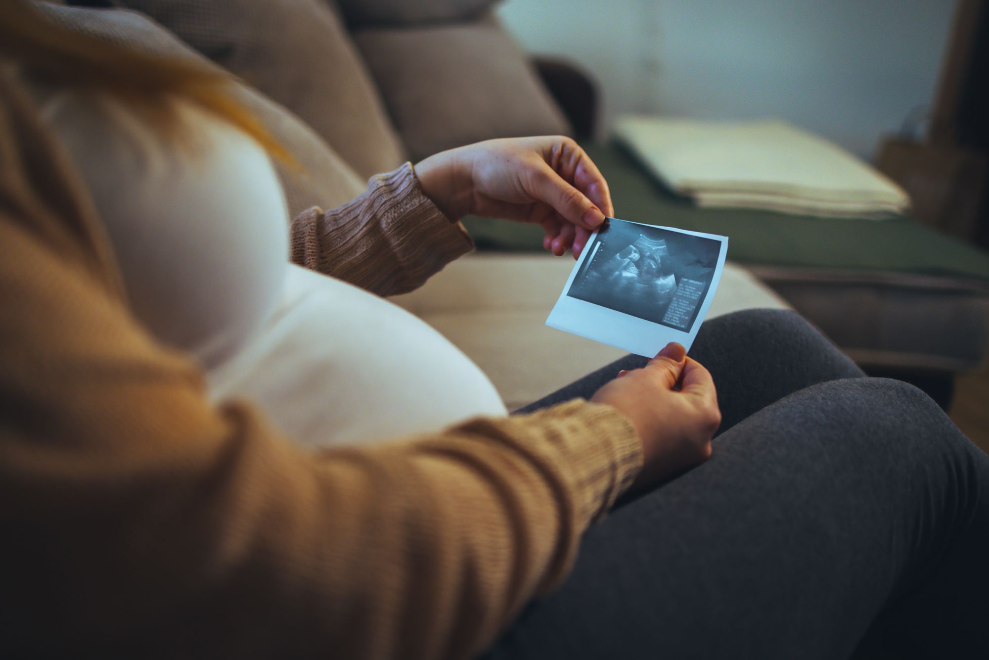 Pregnant woman keeping hand on belly and holding ultrasound image