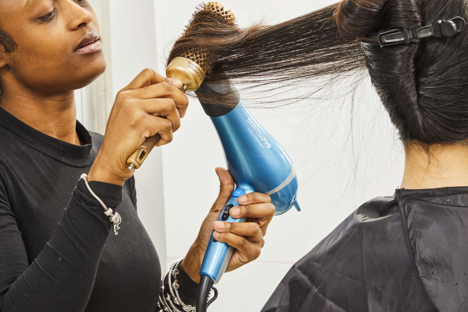 Closeup of a person using a brush and BaBylissPRO Nano Titanium Dryer on another person's hair