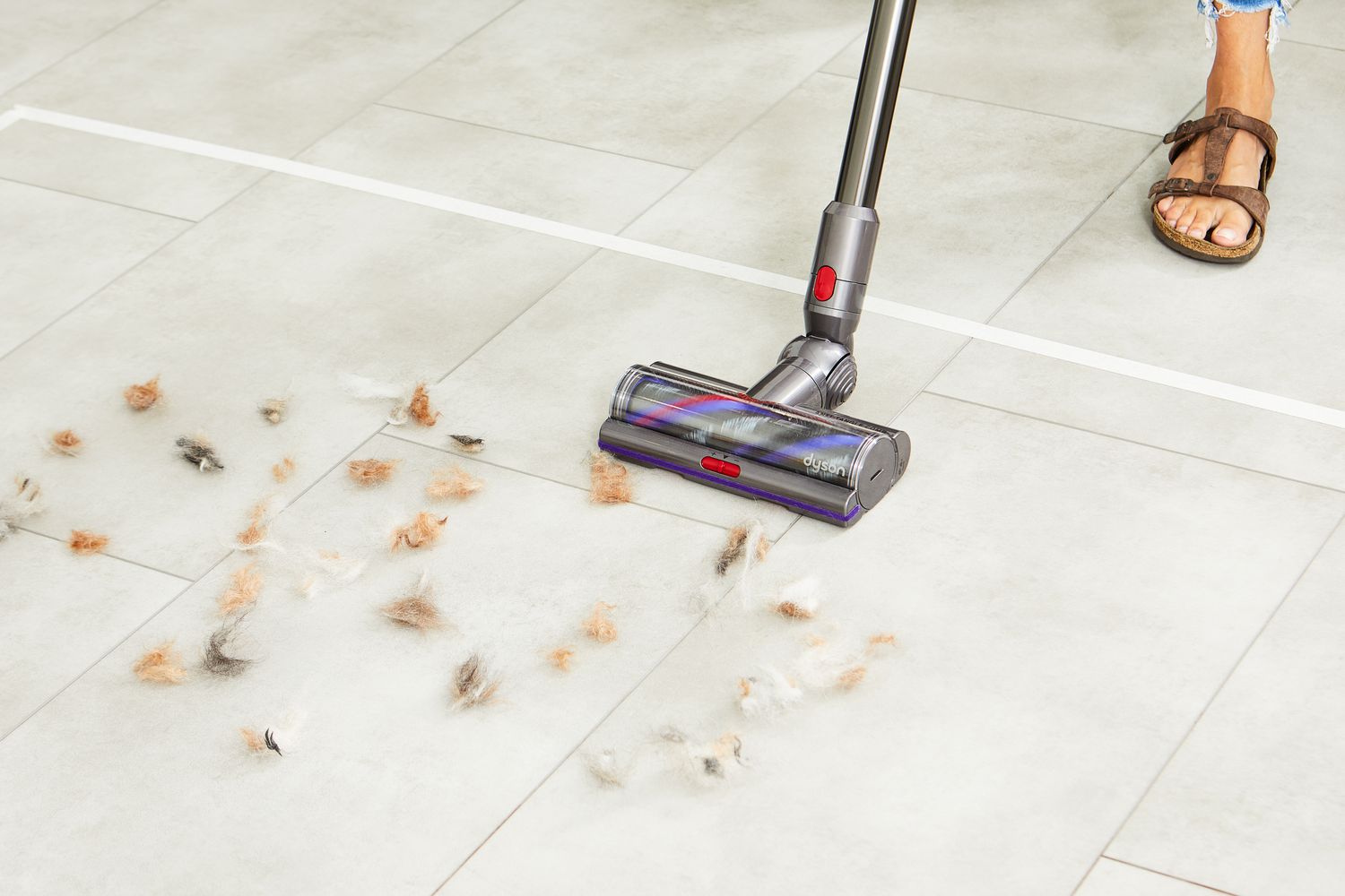 Person using Dyson Cyclone V10 Animal Cordless Stick Vacuum to clean fur from tile floor
