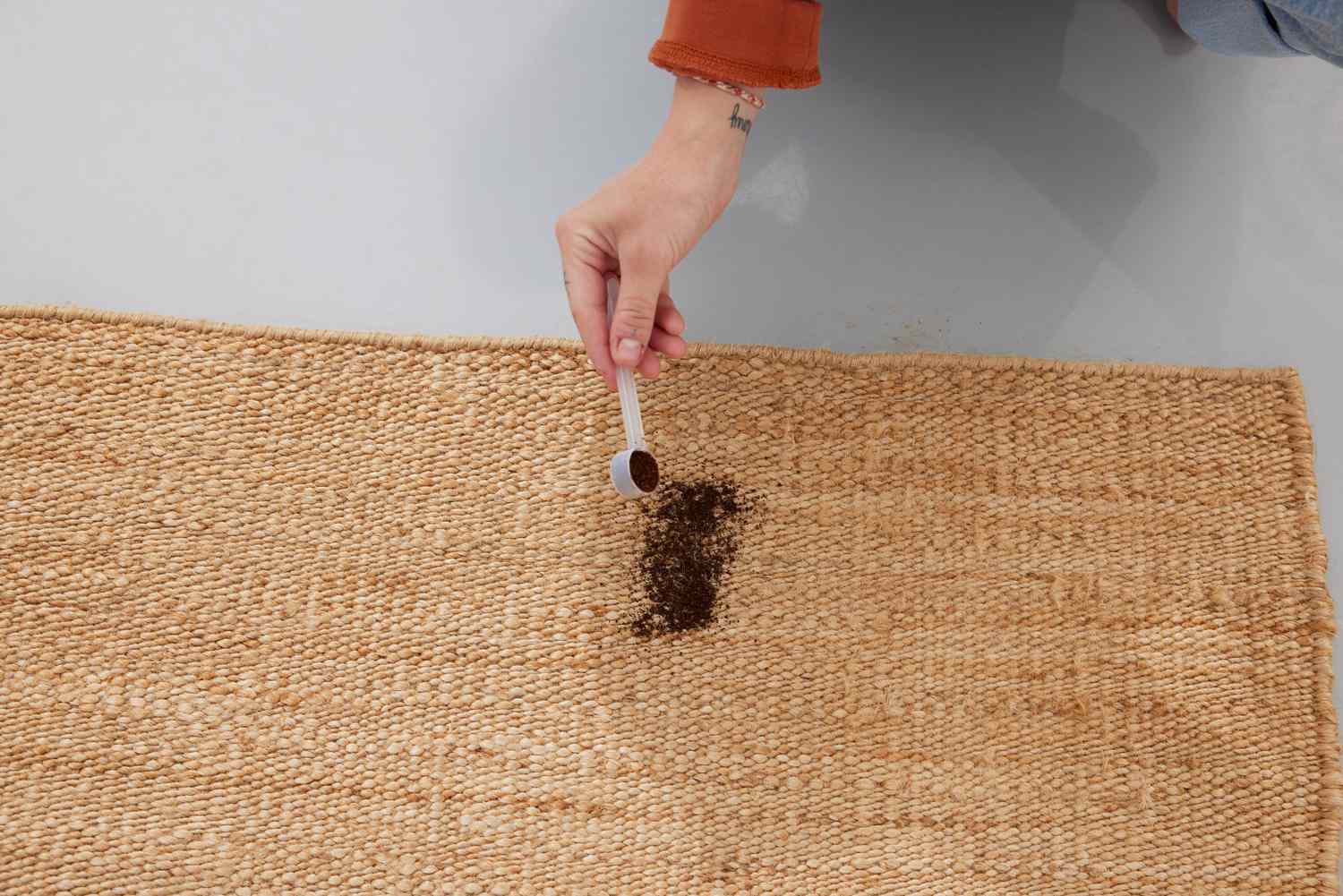 A person places coffee grounds on the Revival Hart Jute Rug