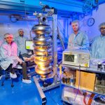 Fermilab engineers and Department of Atomic Energy visitors pause work to pose next to a 5-cell 650 MHz superconducting radio frequency cavity