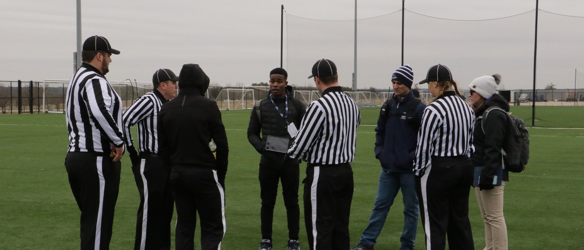 group of officials and other staff in a circle talking on a field