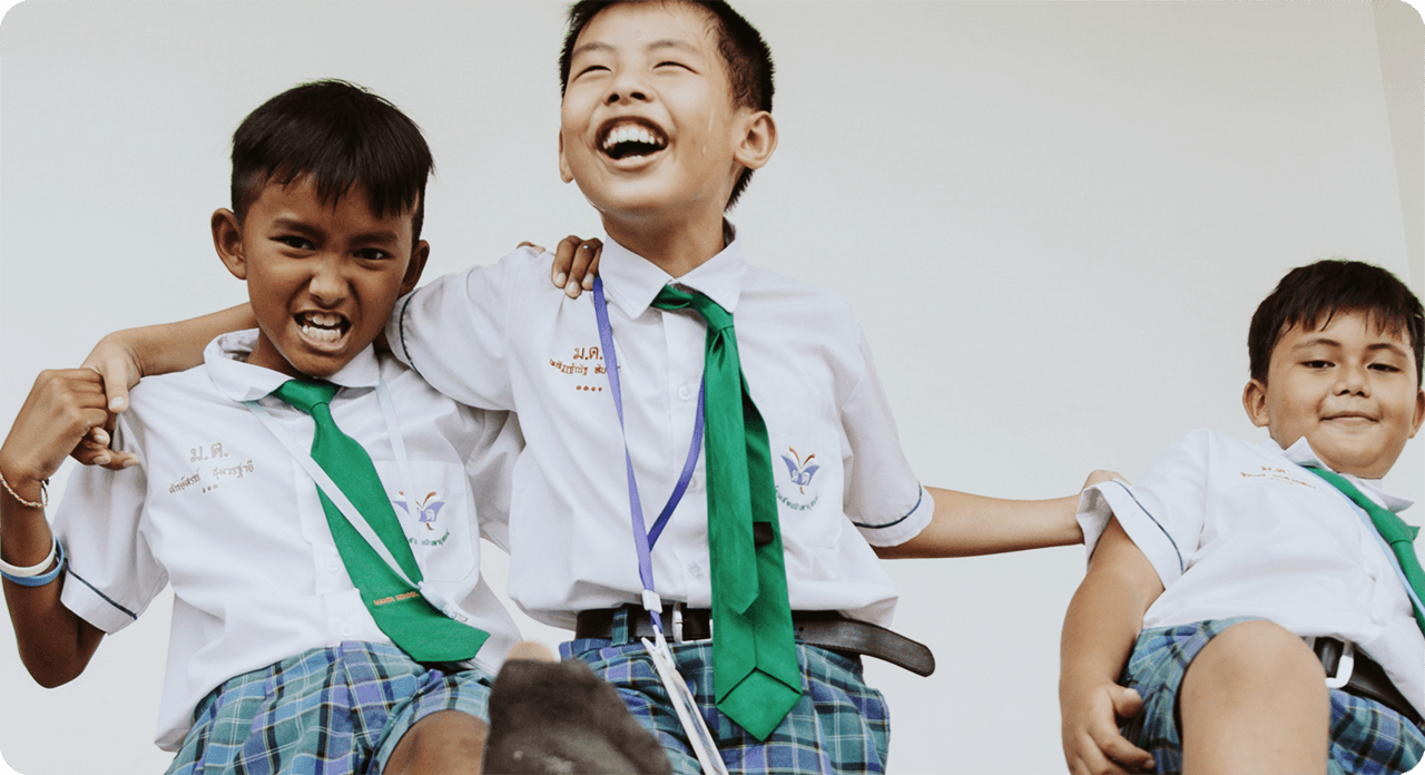 3 smiling, young boys from Thailand wearing school uniforms and playing