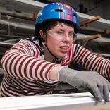 A woman with a disability wearing a helmet works in a factory