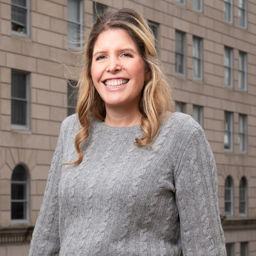 Headshot of a smiling adult woman sitting in front of a city backdrop