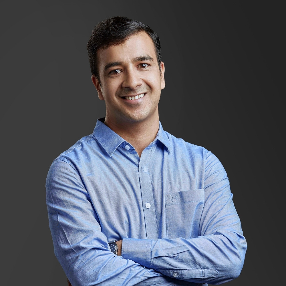 Headshot of an adult man standing with his arms crossed in front of a grey background