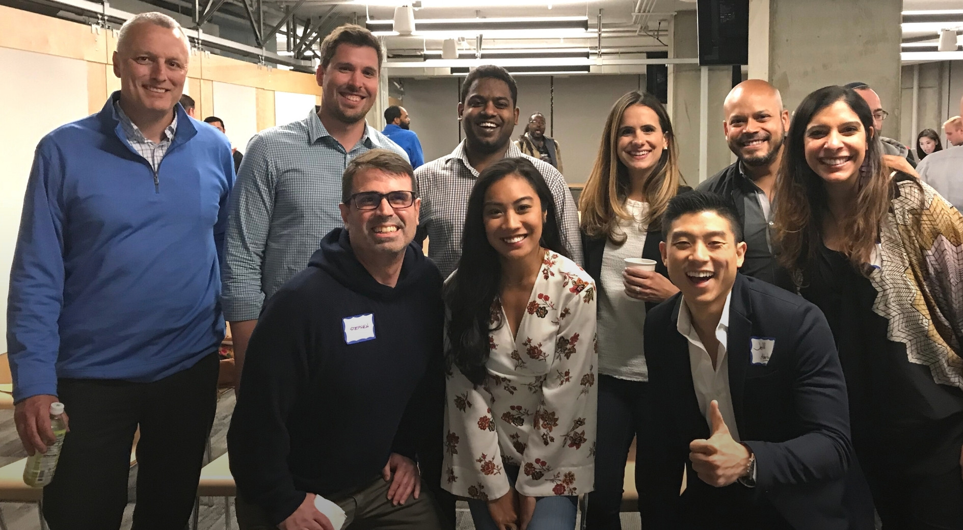 Nine smiling adults posing together in a building