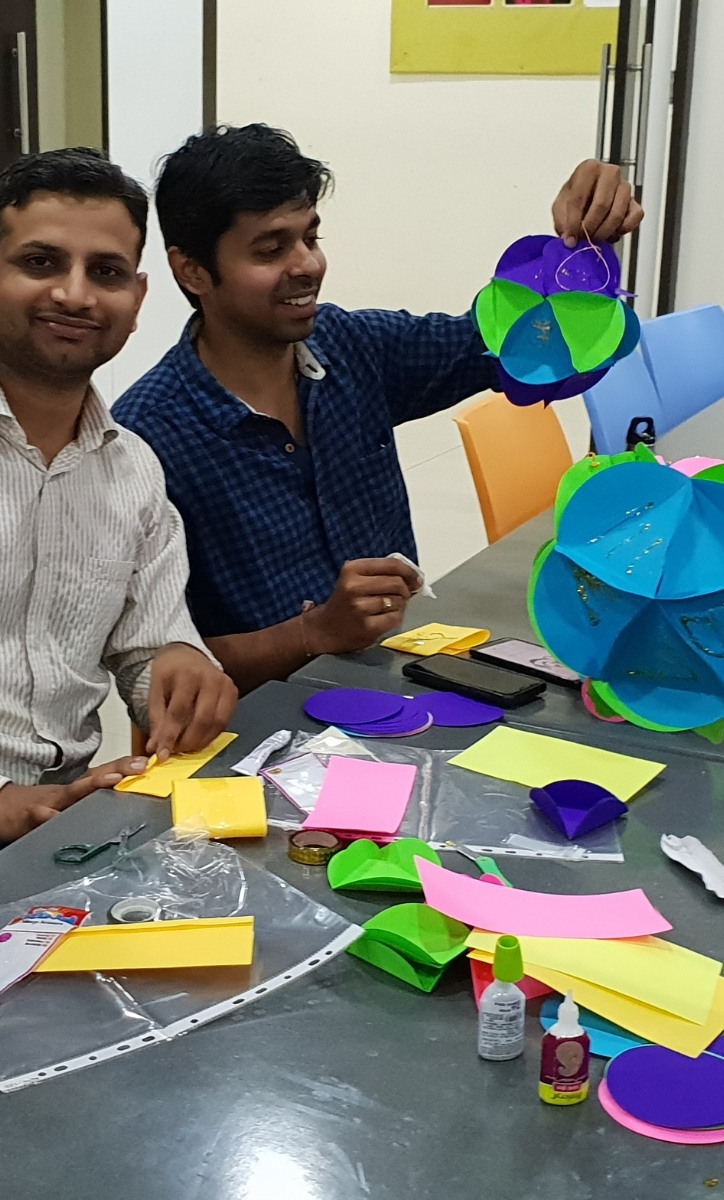 Two adult men sitting at a table. There are arts and craft supplies in front of them