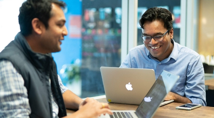 Two smiling adult men working in an office space on their laptops