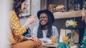 Three smiling woman seated at a cafe enjoying their drinks.