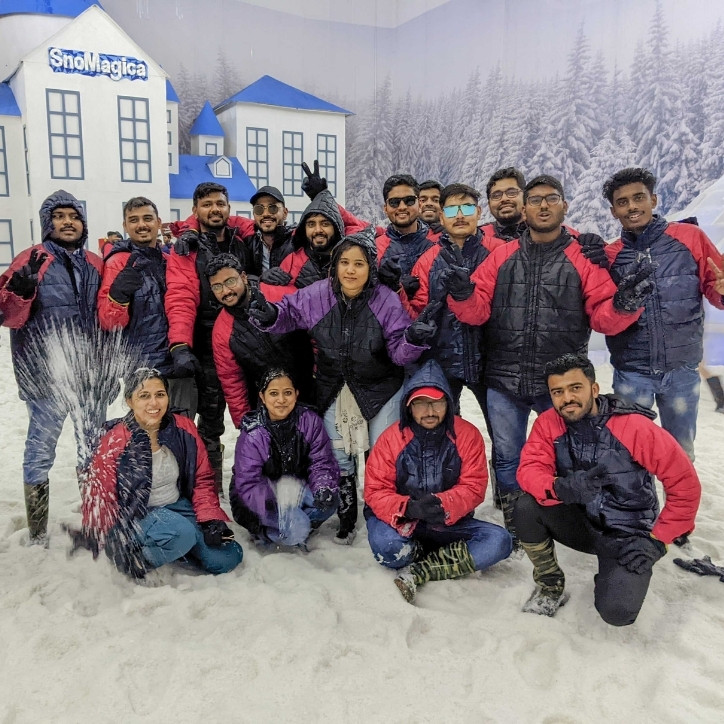 Four PubMatic employees kneeling on the snow and thirteen standing outside with a backdrop of a forest behind them. There is also a castle with the text " SnoMagica" over it