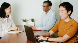 Woman smiling on her laptop with two co-workers talking in the background