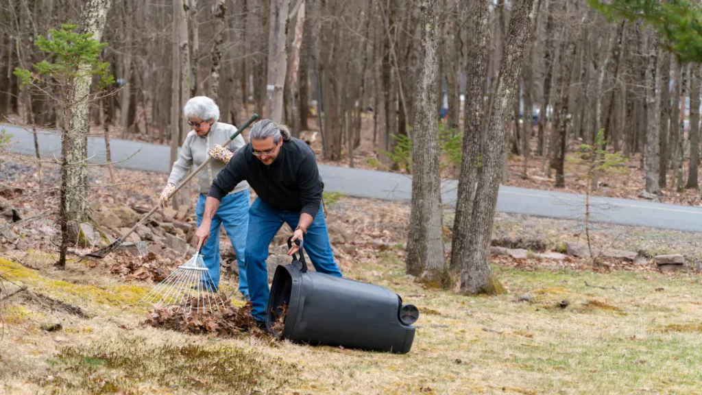 people gathering leaves into a trash can