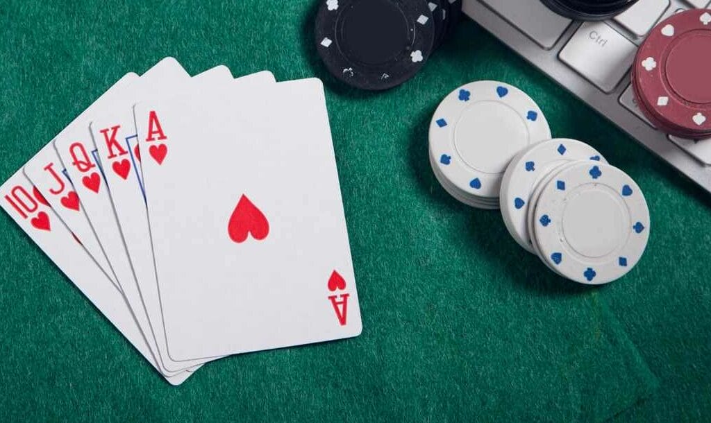 A royal flush poker hand sits next to a keyboard with poker chips on it