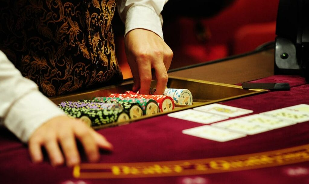 A poker dealer’s hands prepare chips at a red casino table with playing cards and casino chips.