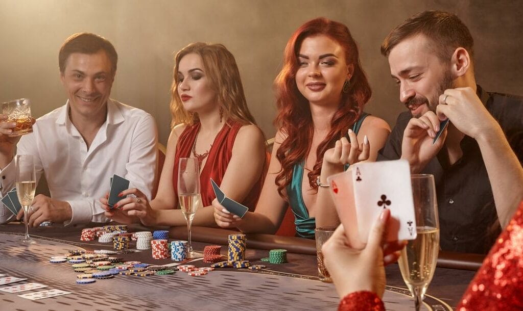 A group of well-dressed men and women playing poker and enjoying drinks at a poker table.