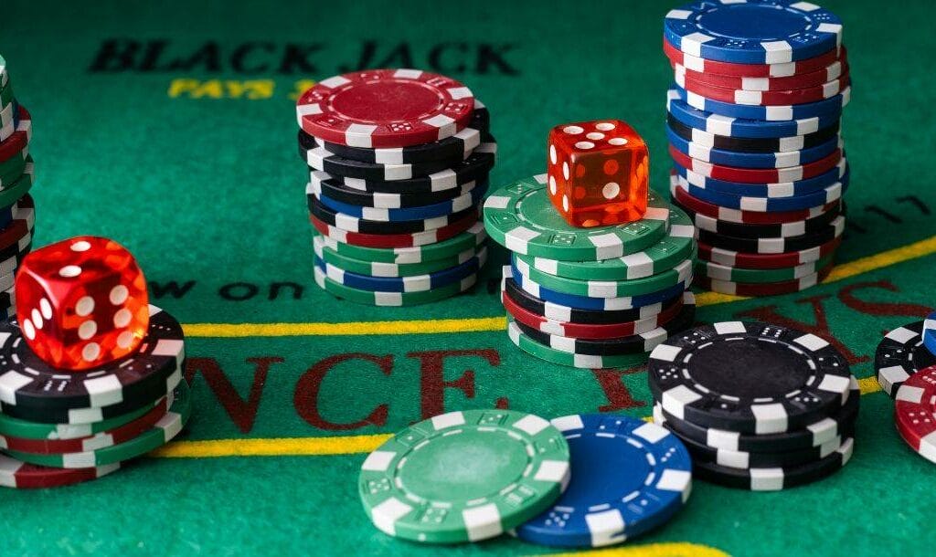 Stacks of black, red, blue, and green poker chips, and a red dice, arranged on a poker table.