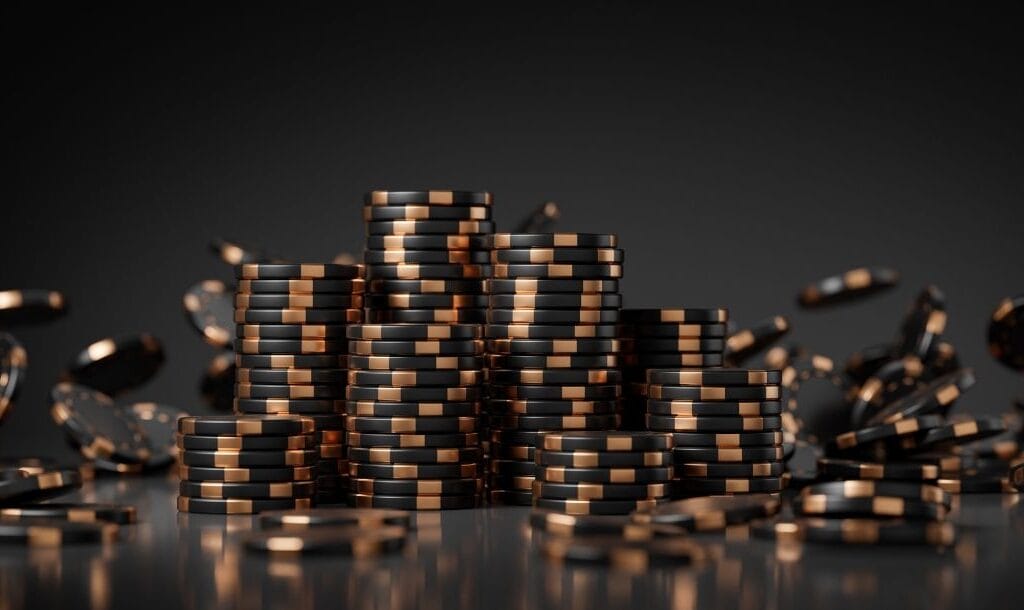 Black and gold poker chips on a black reflective table against a black background.