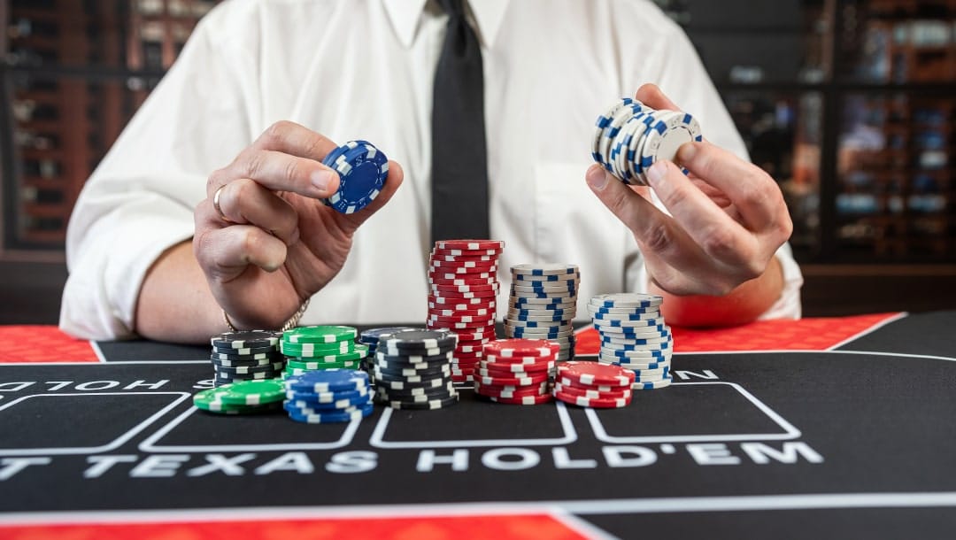 A man wearing a white shirt and black tie holding casino chips on a black and red poker table.