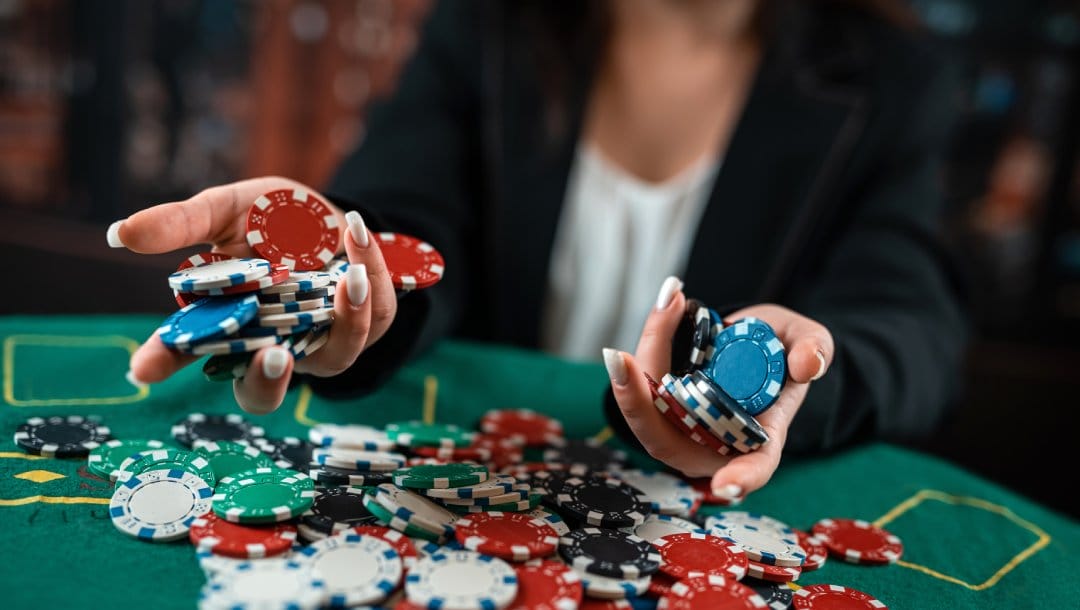 A woman holding casino chips on a poker table with more casino chips displayed.