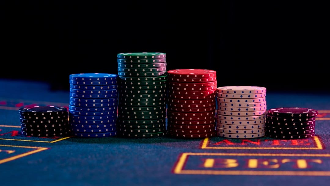 Red, blue, white, and black casino chips on a blue felt poker table.