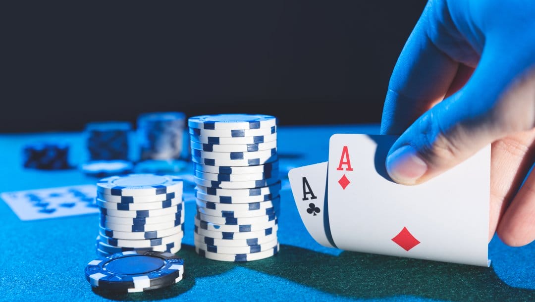 A hand holding two Ace playing cards with white and black casino chips.