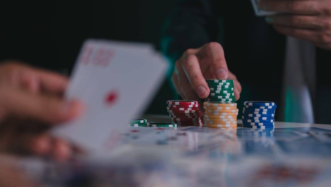 Hands holding playing cards and casino chips on a poker table.