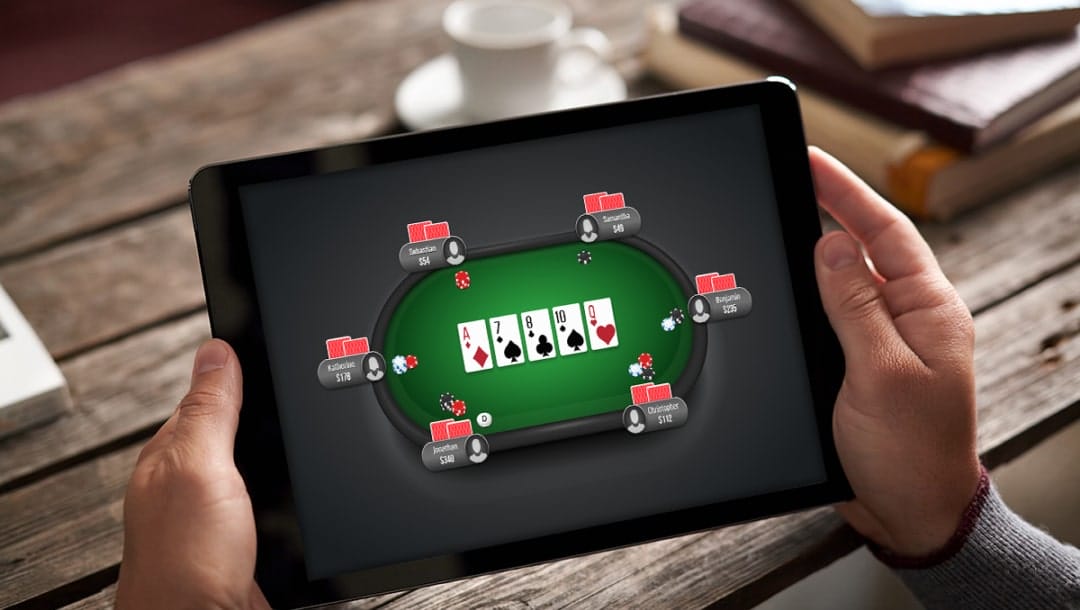 Hands holding a tablet device with an online poker game on the screen.