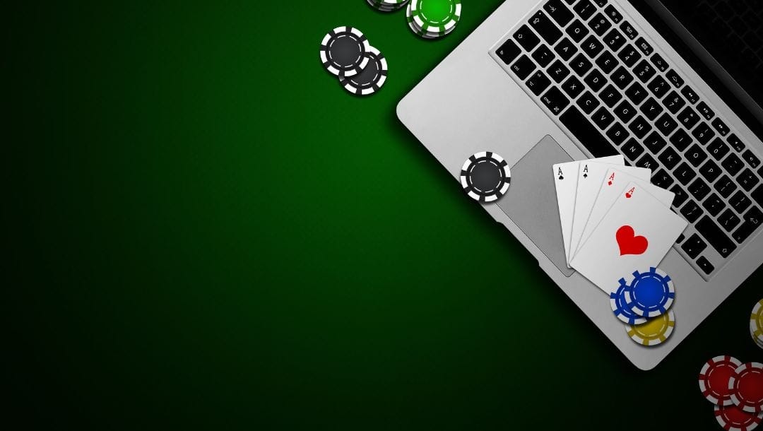 A laptop, poker chips, and playing cards, arranged on a green table.