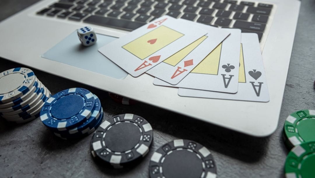 A laptop, poker chips, and playing cards, arranged on a green table.