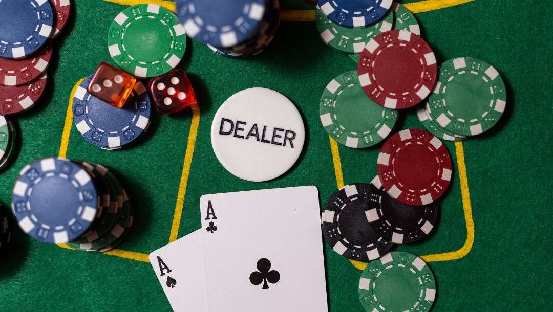 An ace of spades, and an ace of clubs, a dealer chips, and different colored poker chips arranged on a poker table.