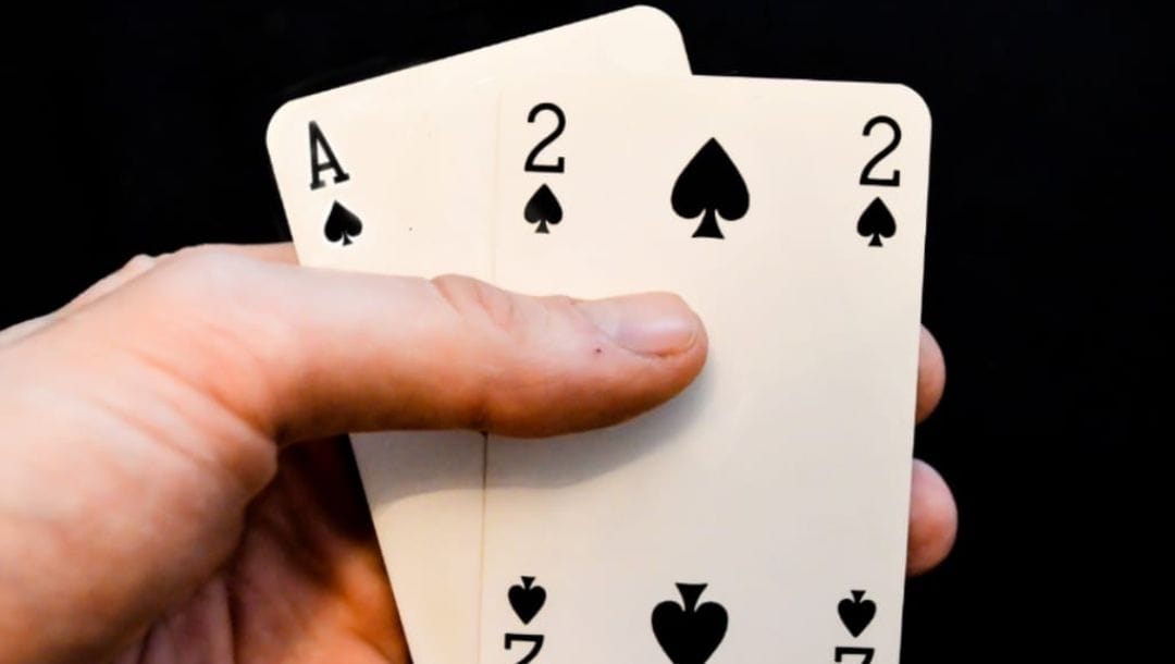 An extreme closeup of a hand holding A-2 suited, in the spades suit, against a black backgound.