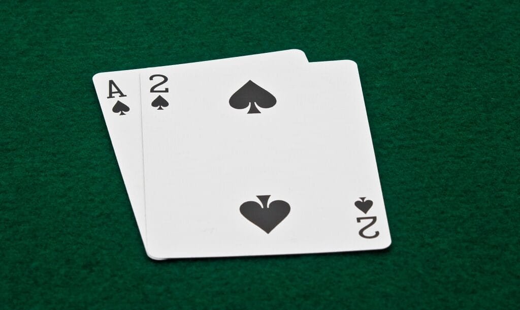 A photograph of an Ace and a Two of Spades (A-2 Suited) on a green felt poker table.