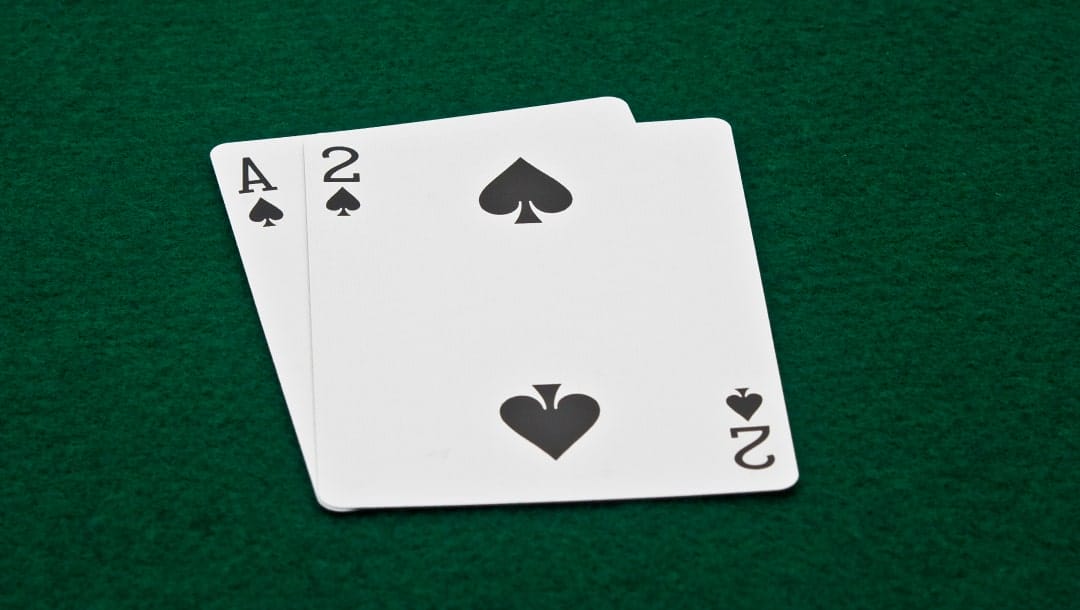 A photograph of an Ace and a Two of Spades (A-2 Suited) on a green felt poker table.