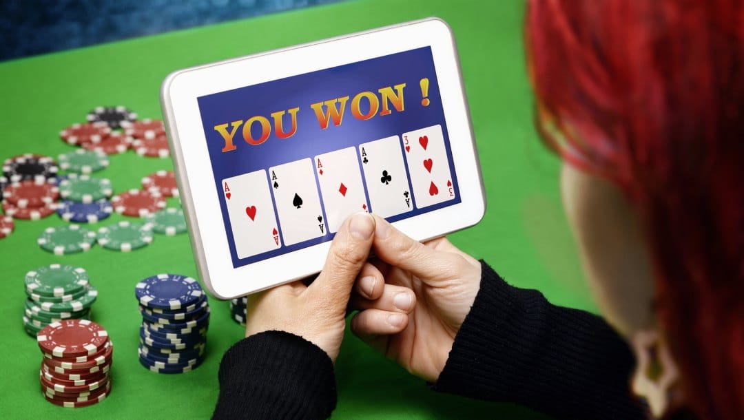 A woman playing a casino game with playing cards on a tablet device. The woman is sitting at a green felt casino table with casino chips.