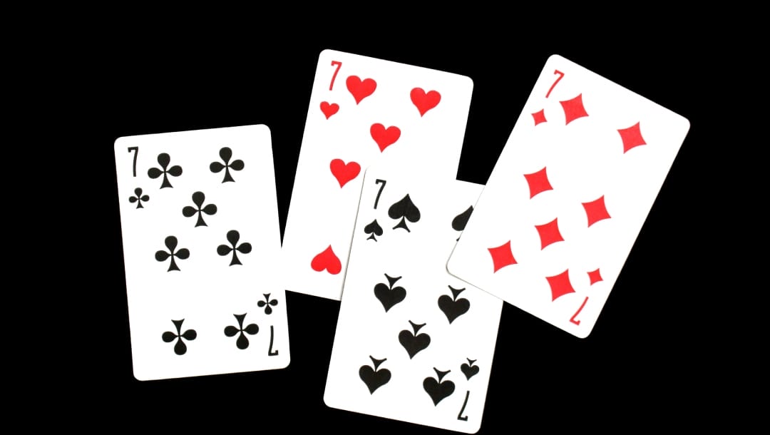 Four playing cards with the number seven against a black surface. Each playing card suit, including clubs, spades, diamonds, and hearts, is shown.