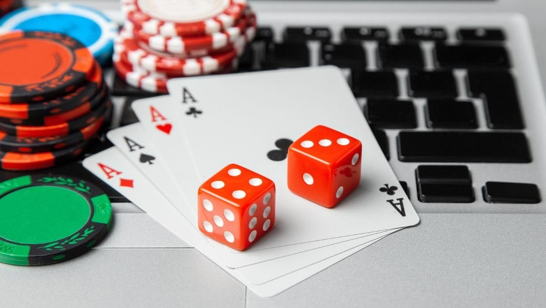 A photograph of two red dice on top of four Ace cards which are fanned out on a laptop keyboard with poker chips next to them.