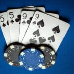 A five of spades, a five of clubs, a nine of spades, and a nice of clubs, arranged on a blue table, featuring two black casino chips, and one blue casino chip.