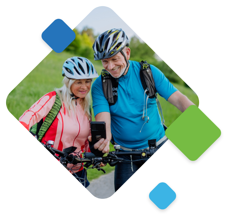 An image of a senior couple in athletic outfits and helmets, holding their bike handles while looking at a cell phone.