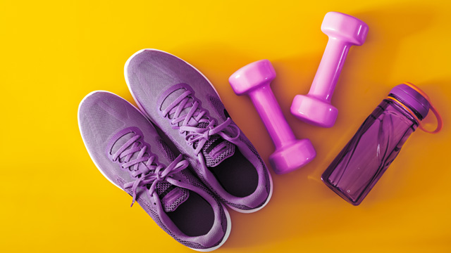 Purple shoes, weights and a water bottle are seen in a top-down view on a bright yellow background