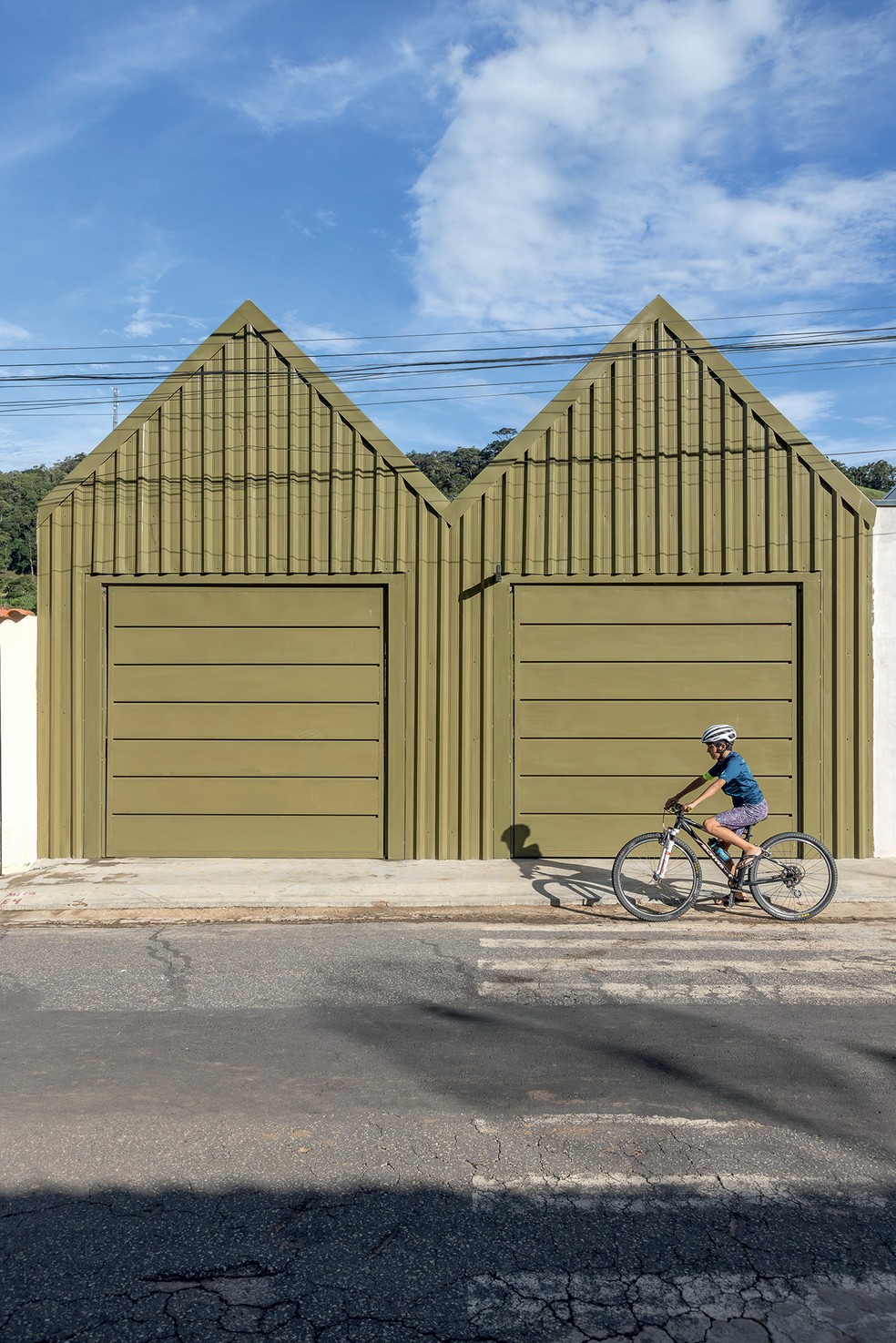 FACHADA | Na outra rua, a edícula feita de telhas-sanduíche serve para a entrada da garagem e se integra com a paisagem por causa da cor — Foto: Evelyn Müller / Divulgação