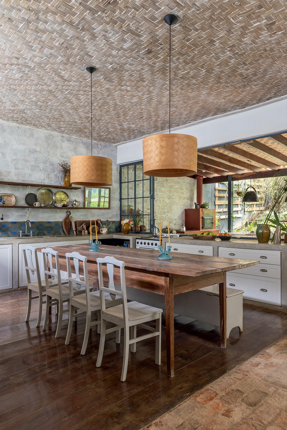 COZINHA | A cozinha de estar tem piso de madeira de demolição arrematada de uma casa próxima, assim como o tampo da mesa. Já as cadeiras, com mais de 80 anos, vieram da casa da avó da proprietária. Acima da bancada de alvenaria com marcenaria da Guará Planejados, o azulejo assinado por Calu Fontes serviu de base para a paleta de cores da casa. O forro de taquara, executado por Fubá e família, recebeu luminárias pendentes da Tok&Stok, além de spots da Reka — Foto: Evelyn Müller / Divulgação