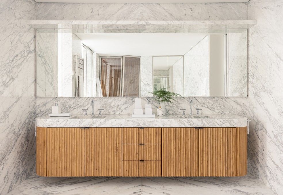 No banheiro da suíte do casal, o mármore Carrara, da Arthus, foi usado tanto nas paredes e no piso quanto na bancada do gabinete de freijó natural maciço — Foto: Fran Parente