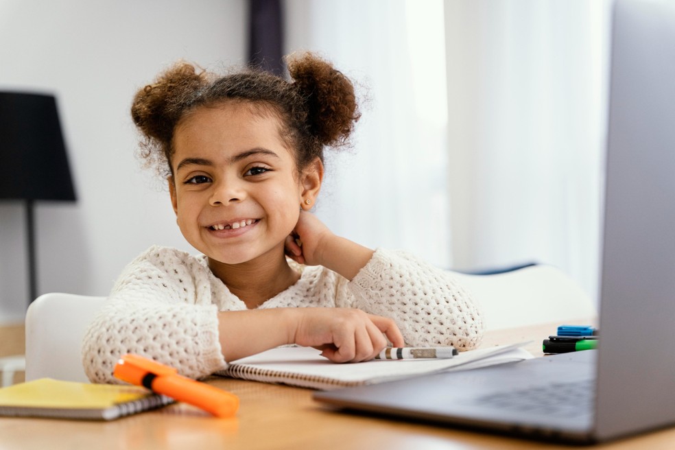 Menina sorrindo enquanto faz a lição de casa — Foto: Freepik